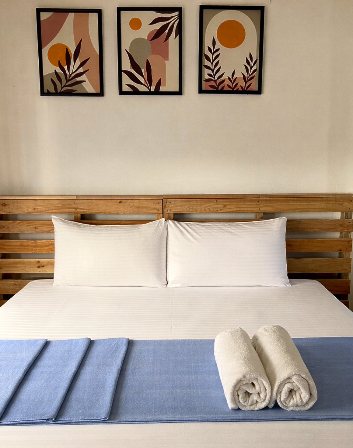 Creative Double Room — clean white pillows on a wooden headboard, three sun-and-leaf prints above the bed