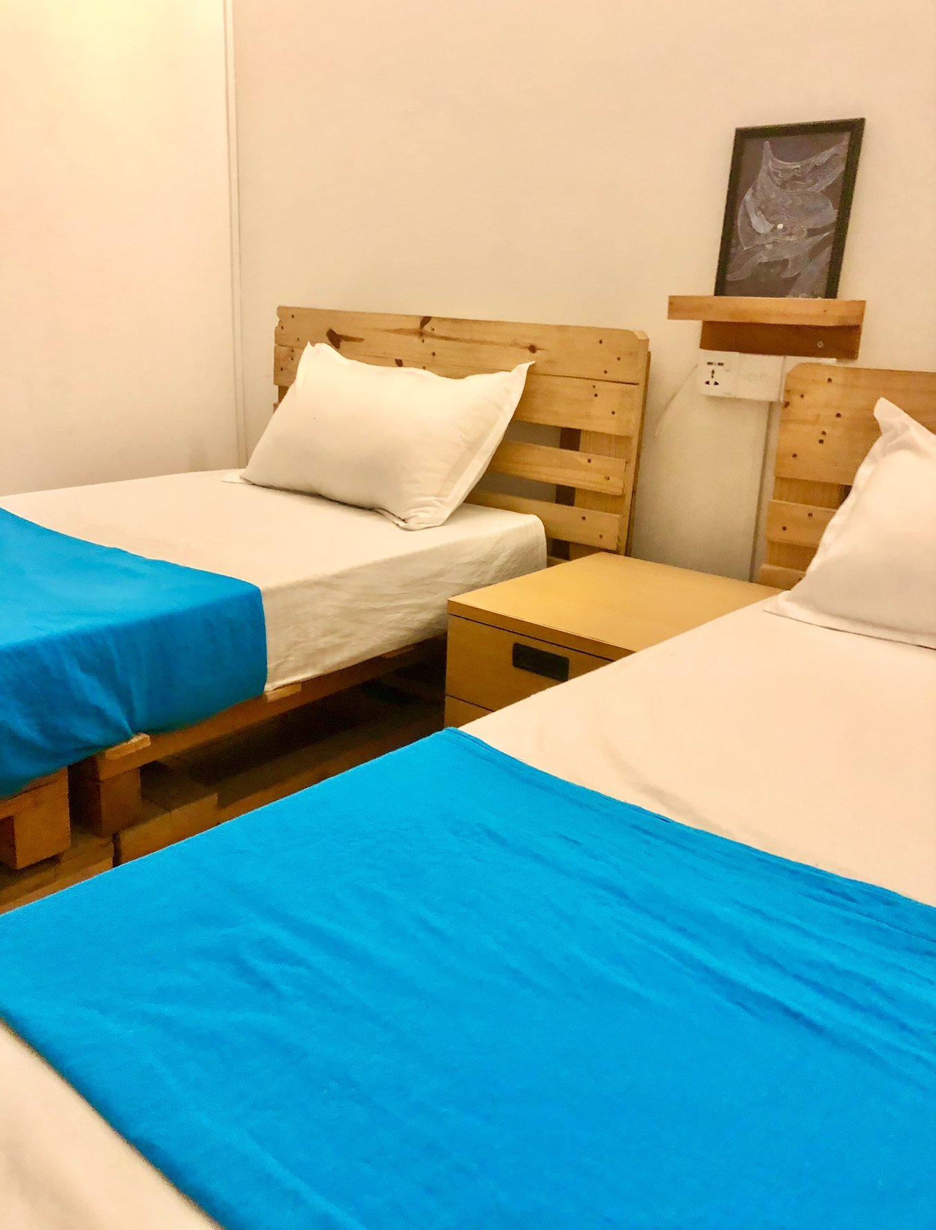 Waves Single Room at Seconds Colombo — twin pallet beds with bright blue runners, neutral walls, a single black-framed artwork